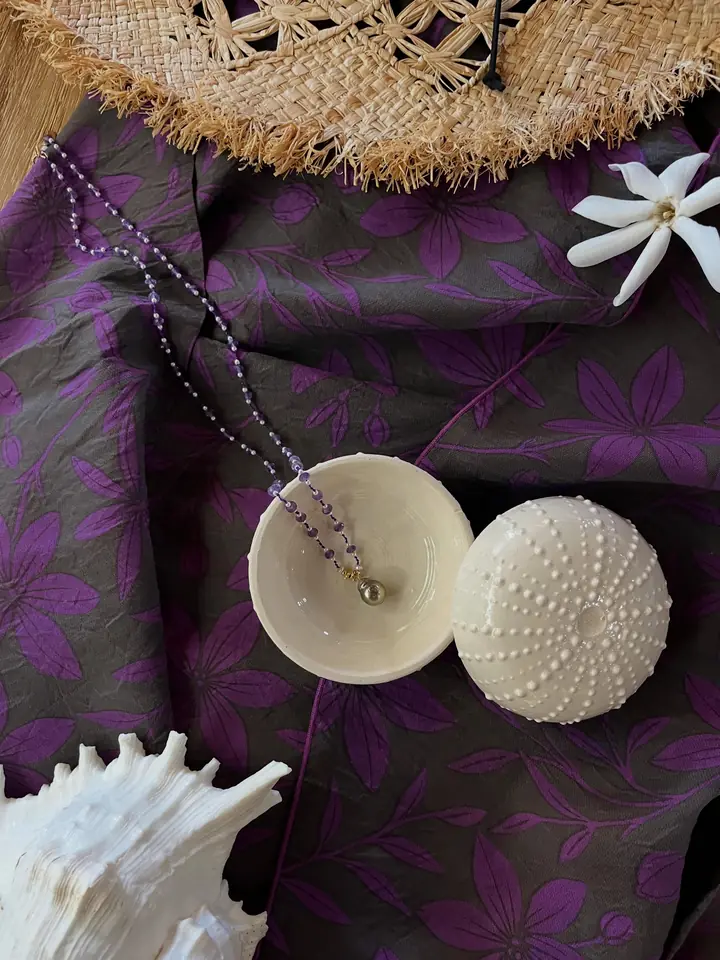Chapeau de paille, coquillages et collier sur un pāreu violet
