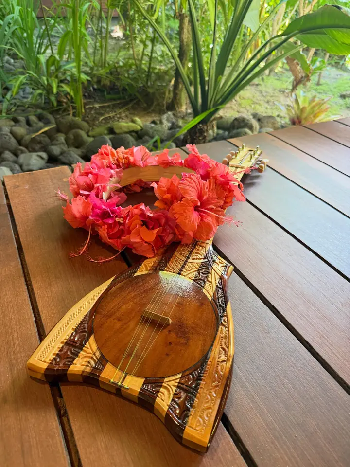 ʻUkulele tahitien posé sur un pāreu, avec une couronne de fleurs